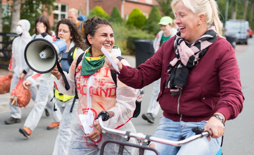 young smiling climate activist woman giving a folder to older smiling lady on a bicycle