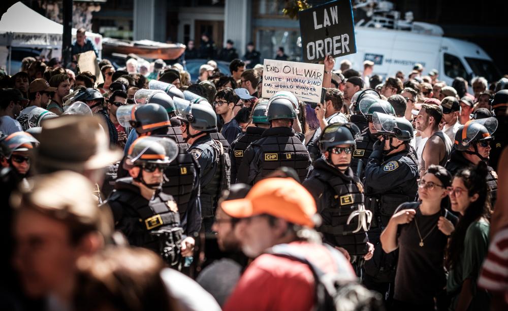Protester amongst police - placard reading: End Oil War