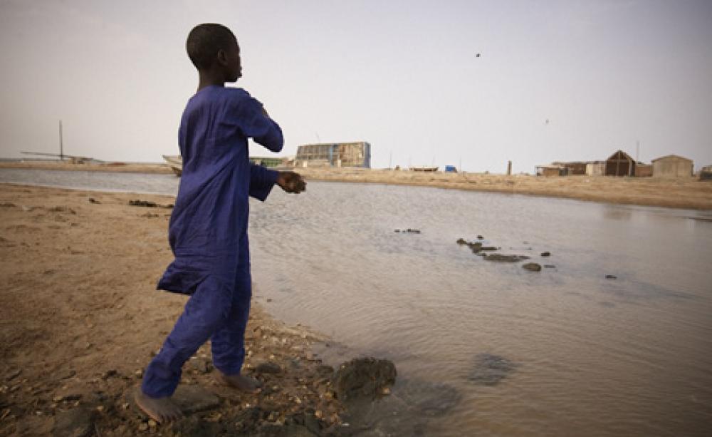 A boy skims a stone on the water covering his former school