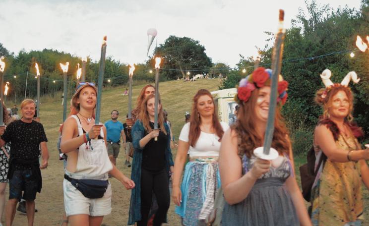Summer evening parade at Timber Festival with long candle torches burning.